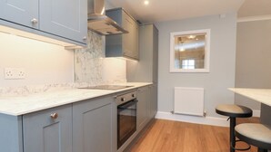 A modern kitchen with grey cabinets, a marble countertop, a built-in oven, and a window with a view.