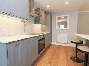 A modern kitchen with grey cabinets, a marble countertop, a built-in oven, and a window with a view. - Marilyn (Morecambe)