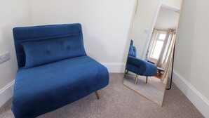 A room with a blue sofa, a full-length mirror, and a carpeted floor.