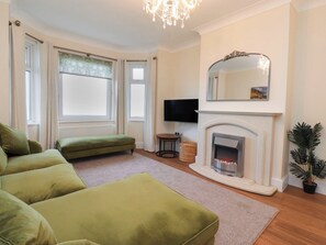 Una sala de estar con chimenea, sofá verde y televisor.