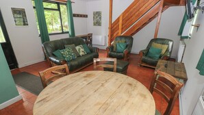 A living room with a round wooden table, leather sofas, and wooden chairs. - Cabin No. 12 - Salt and Fern Cabins (Port Talbot)