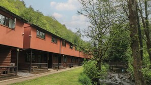 A building with a red exterior, multiple windows, and a covered outdoor area with benches. - Cabin No. 12 - Salt and Fern Cabins (Port Talbot)