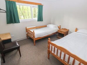 A room with two wooden beds, a wooden nightstand, a wooden chair, and a window with green curtains. - Cabin No. 12 - Salt and Fern Cabins (Port Talbot)