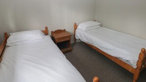 A small, clean room with two wooden beds, a nightstand, and a carpeted floor. - Cabin No. 12 - Salt and Fern Cabins (Port Talbot)