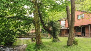 A rustic cabin with a pond, surrounded by lush greenery and a wooden fence. - Cabin No. 12 - Salt and Fern Cabins (Port Talbot)