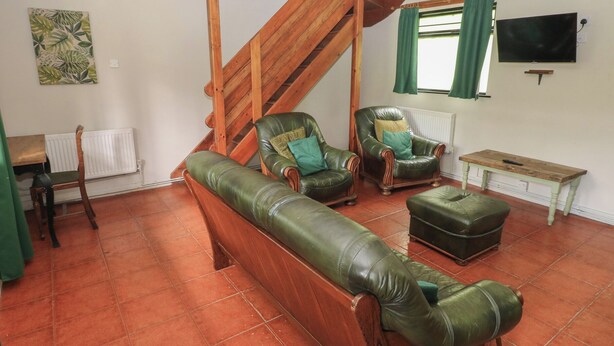 A living room with a wooden staircase, leather sofas, a wooden table, and a television. - Cabin No. 12 - Salt and Fern Cabins (Port Talbot)