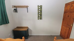A bedroom with two wooden beds, a wooden dresser, a coat rack, and a door. - Cabin No. 12 - Salt and Fern Cabins (Port Talbot)