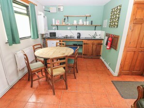 A kitchen with a round wooden table, chairs, a refrigerator, a microwave, a kettle, and a fire extinguisher. - Cabin No. 12 - Salt and Fern Cabins (Port Talbot)