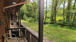 A wooden deck with wicker chairs, a bench, and a railing overlooking a grassy area with trees. - Cabin No. 12 - Salt and Fern Cabins (Port Talbot)