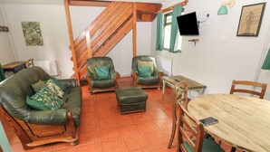 A cozy living room with a green sofa, two armchairs, a wooden dining table, and a staircase. - Cabin No. 12 - Salt and Fern Cabins (Port Talbot)