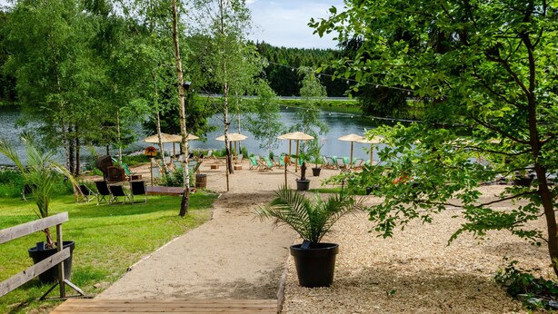 A lakeside patio with outdoor seating, a wooden deck, and potted plants. - Apartment 'Lubeca' with Loggia (Goslar)