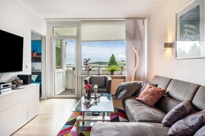Un salon moderne avec un canapé, une table basse en verre, un téléviseur et un balcon offrant une vue agréable.