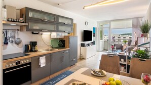A modern kitchen with a dining area, a flat-screen TV, and a view of the city. - Apartment 'Lubeca' with Loggia (Goslar)
