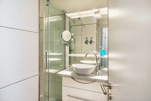 Une salle de bain moderne avec une douche à parois de verre, un lavabo blanc et un miroir.