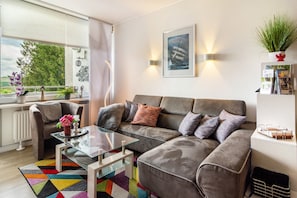 Ein modernes Wohnzimmer mit einem grauen Sofa, einem Glastisch und einem farbenfrohen Teppich.