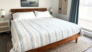 Ein Schlafzimmer mit Bett, Nachttischen, einer Wand-Klimaanlage, einem Fenster mit Vorhängen und einem gerahmten Bild an der Wand.