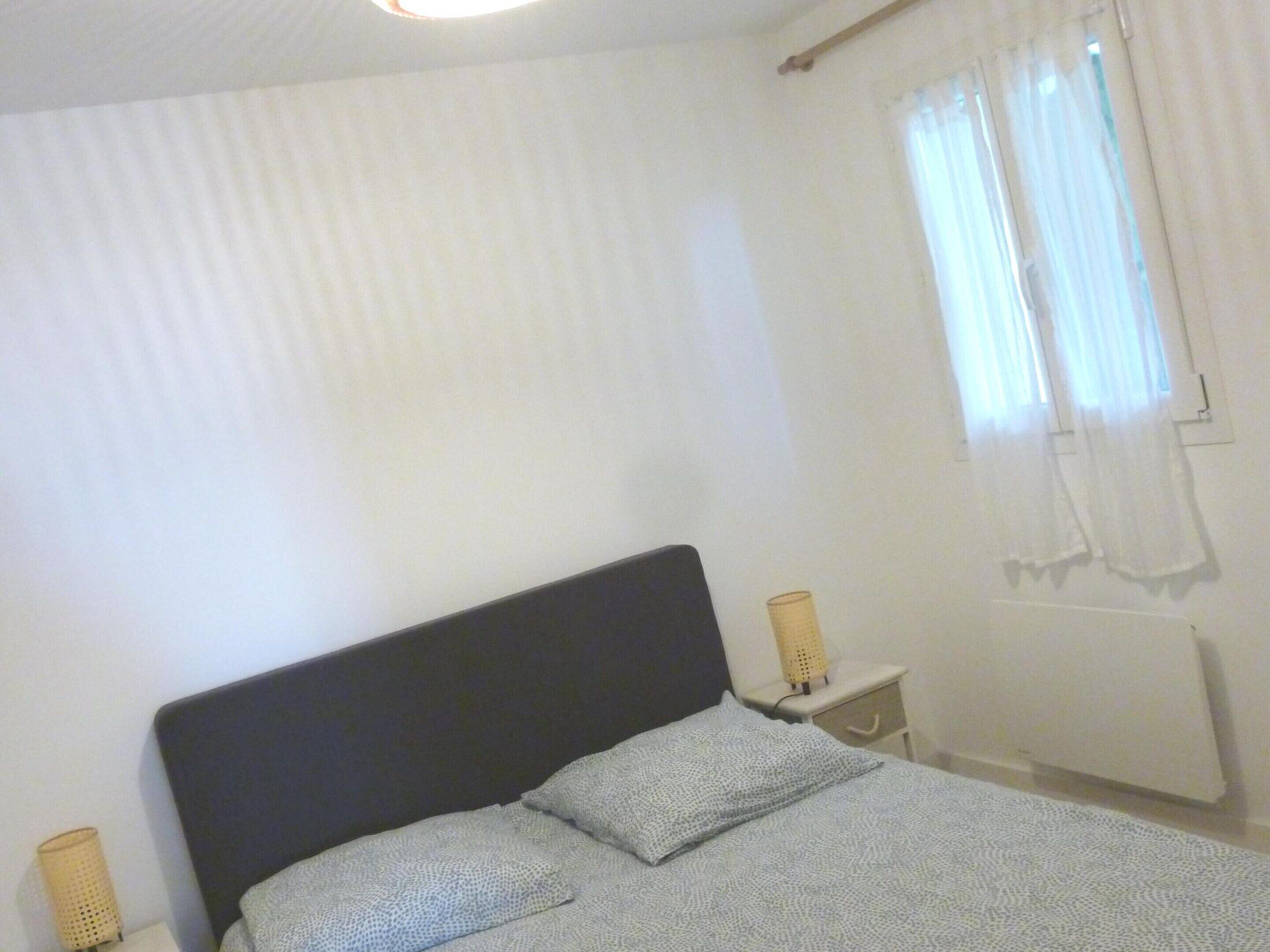 Et soveværelse med seng, to sengeborde med lamper, et vindue med gardiner og en radiator.