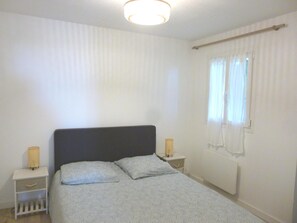 Un dormitorio con una cama, dos mesitas de noche, una ventana con cortinas y una lámpara en el techo.
