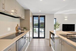 A modern kitchen with a sliding glass door leading to a balcony, built-in appliances, and a flat-screen TV. - Amalfi—Ocean Views & Pool near Beach & Restaurants (Trinity Beach)