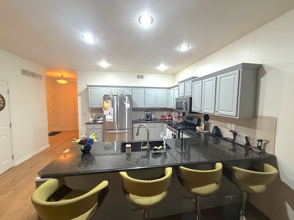 Una cocina moderna con una isla central, taburetes de bar, electrodomésticos de acero inoxidable y armarios de color gris claro.