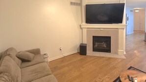 A living room with a sofa, a fireplace, a television, and a ceiling fan. - Azura Amphitheater Home — Sleeps 6 (Kansas City)