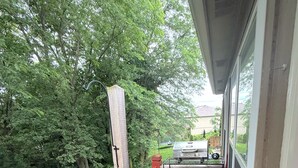 A wooden deck with a red railing, a wicker sofa, and a grill area. - Azura Amphitheater Home — Sleeps 6 (Kansas City)