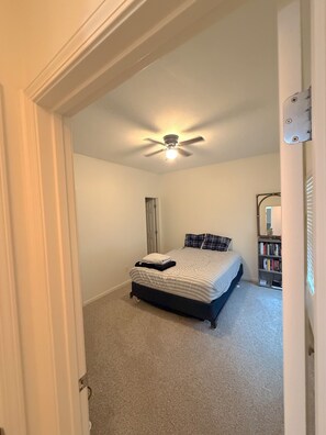 Une chambre à coucher avec un lit, un ventilateur de plafond, une bibliothèque et une porte.