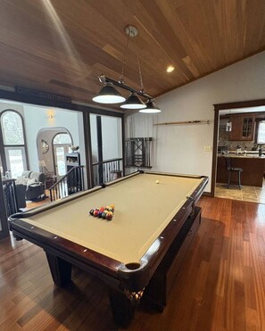 A pool table with balls, a staircase, and a kitchen area.