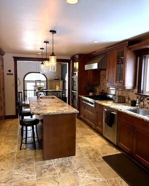 A kitchen with a central island, stainless steel appliances, wooden cabinets, and a chandelier.