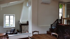 Una habitación con chimenea, una mesa de comedor, sillas, una escalera y un equipo de aire acondicionado.
