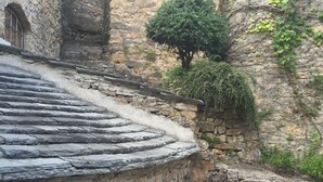 Un edificio de piedra con techo de tejas, un pequeño árbol y un muro de piedra.