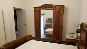 Un dormitorio con una cama de madera, un armario de madera con espejo y una mesita de noche con lámpara.