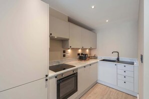 Eine moderne Küche mit weißen Schränken, einem eingebauten Backofen, einem Kochfeld, einer Spüle und einer Dunstabzugshaube.