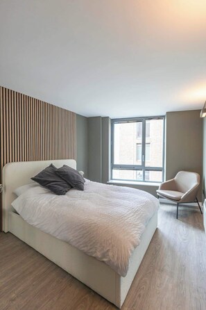 Ein modernes Schlafzimmer mit einem großen Bett, einem Sessel und einem Fenster, das natürliches Licht hereinlässt.