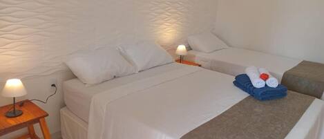 A hotel room with two beds, a nightstand with a lamp, and a towel rack with folded towels.