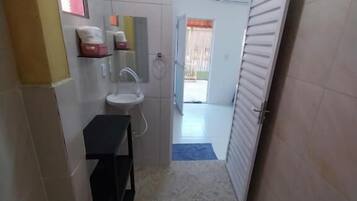 A narrow bathroom with a sink, mirror, and towel rack. A toilet is visible in the corner, and a towel is hanging on the wall.
