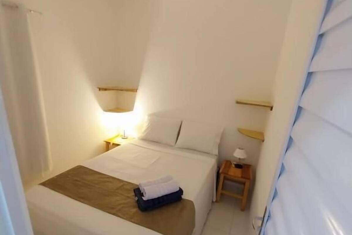 A small, clean hotel room with a single bed, bedside tables, and a window with blinds.