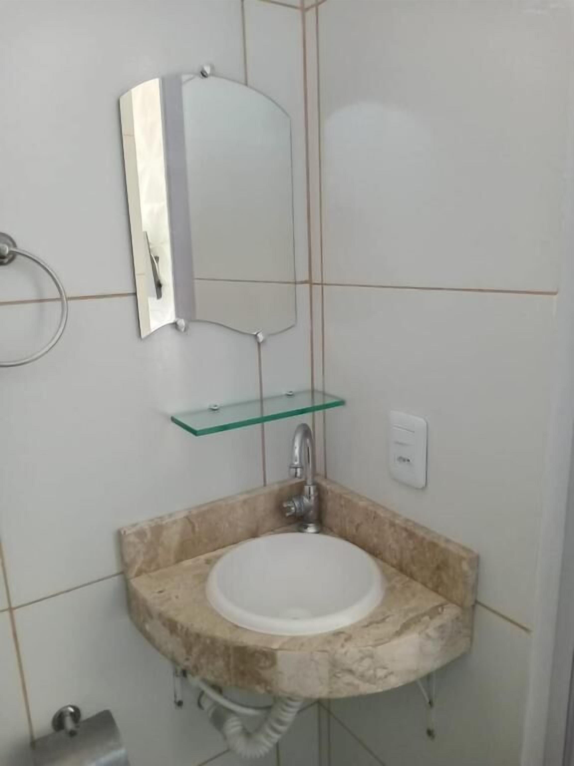 A bathroom with a marble sink, a glass shelf, a mirror, and a toilet.