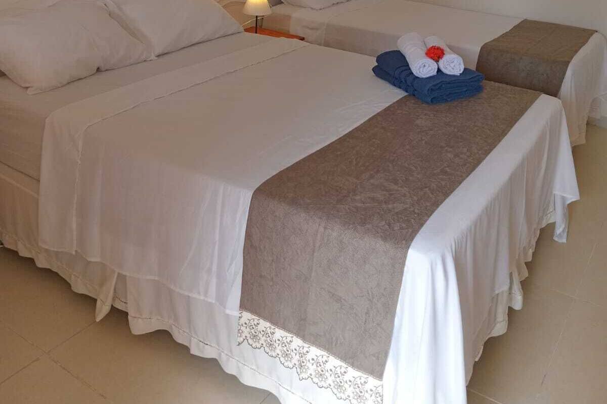 A hotel room with two beds, a nightstand with a lamp, and a neatly made bed with towels and a flower.