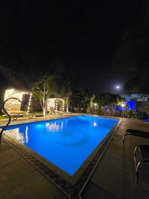 A nighttime swimming pool with lounge chairs and ambient lighting. - Jardim das Dunas (Aracati)