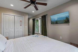 A bedroom with a bed, a ceiling fan, a window with curtains, and a wall-mounted painting. - 7-Bedroom Gatlinburg Cabin with Swim Spa, Sauna & Mountain Views (Gatlinburg)
