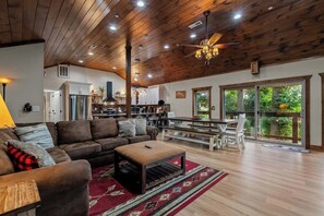 A spacious living area with a wooden ceiling, a large sofa, a dining table, and a kitchen in the background. - Gatlinburg 7BR | Swim Spa + Sauna (Gatlinburg)