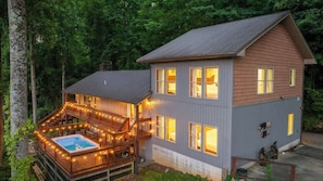 A two-story house with a hot tub on the second floor and a deck with lights. - 7-Bedroom Gatlinburg Cabin with Swim Spa, Sauna & Mountain Views (Gatlinburg)