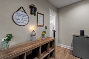 Een gang met een houten bankje, decoraties aan de muur, een deur en een speaker.