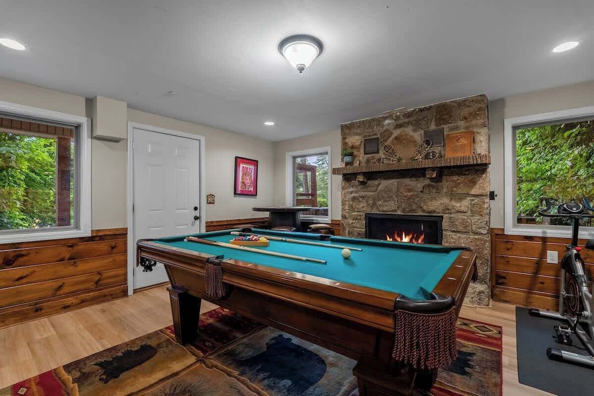 A pool table with a fire feature, a bicycle, and a view of greenery outside.