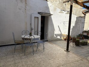 Eine Terrasse im Freien mit einem runden Tisch, Stühlen, Blumentöpfen und einer Tür.