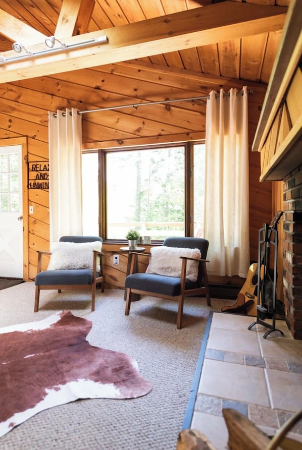 A cozy cabin interior with wooden walls, two chairs, a rug, and a guitar. - Private Cabin 4BR 3BA, Fire pit, Pool table, BBQ Weber, Babbling Brook, Cornhole (Dover)