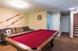 A pool table with a red felt surface, a dartboard, and skis mounted on the wall.