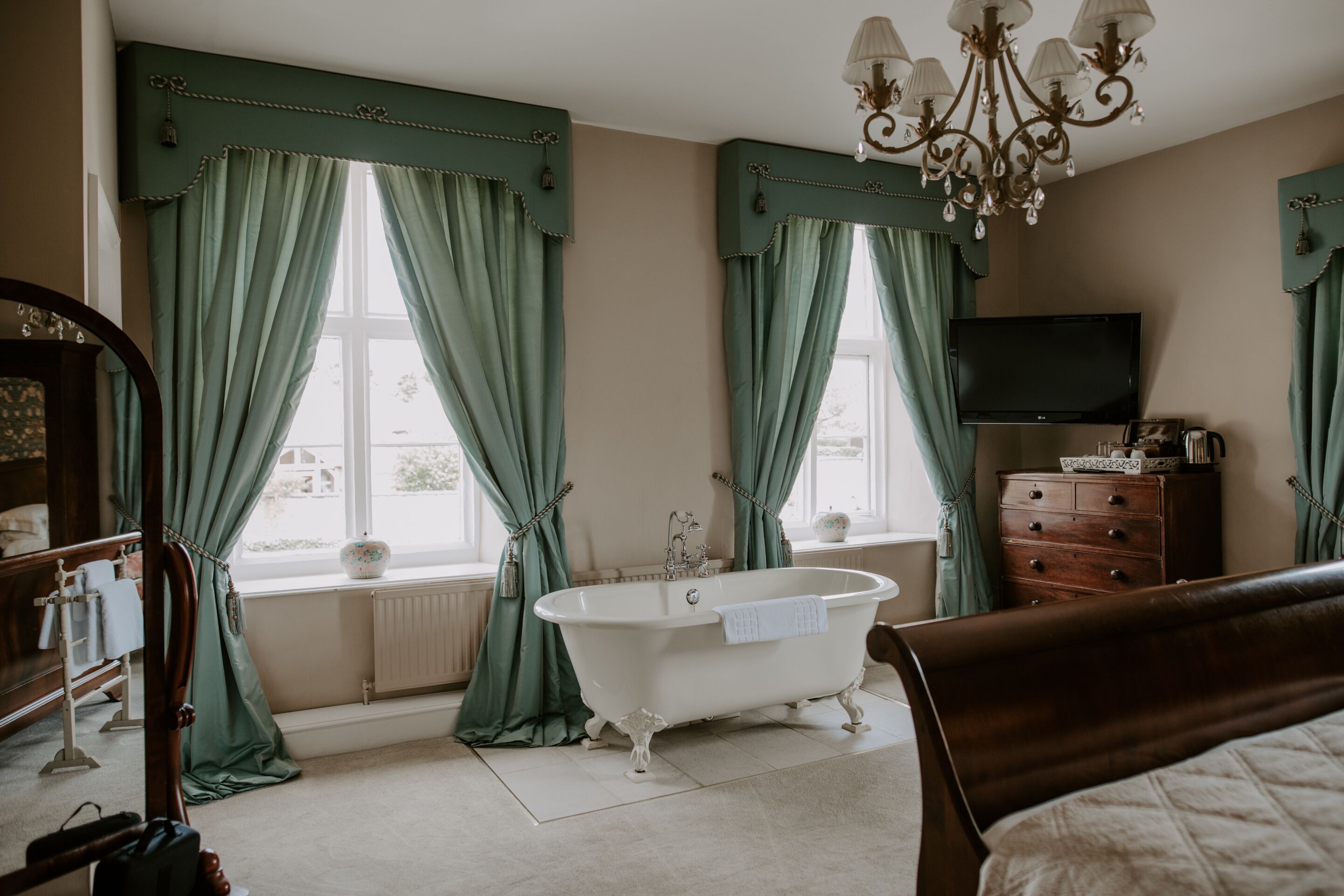 Een kamer met een pootbad, een houten dressoir, een televisie en een kroonluchter.