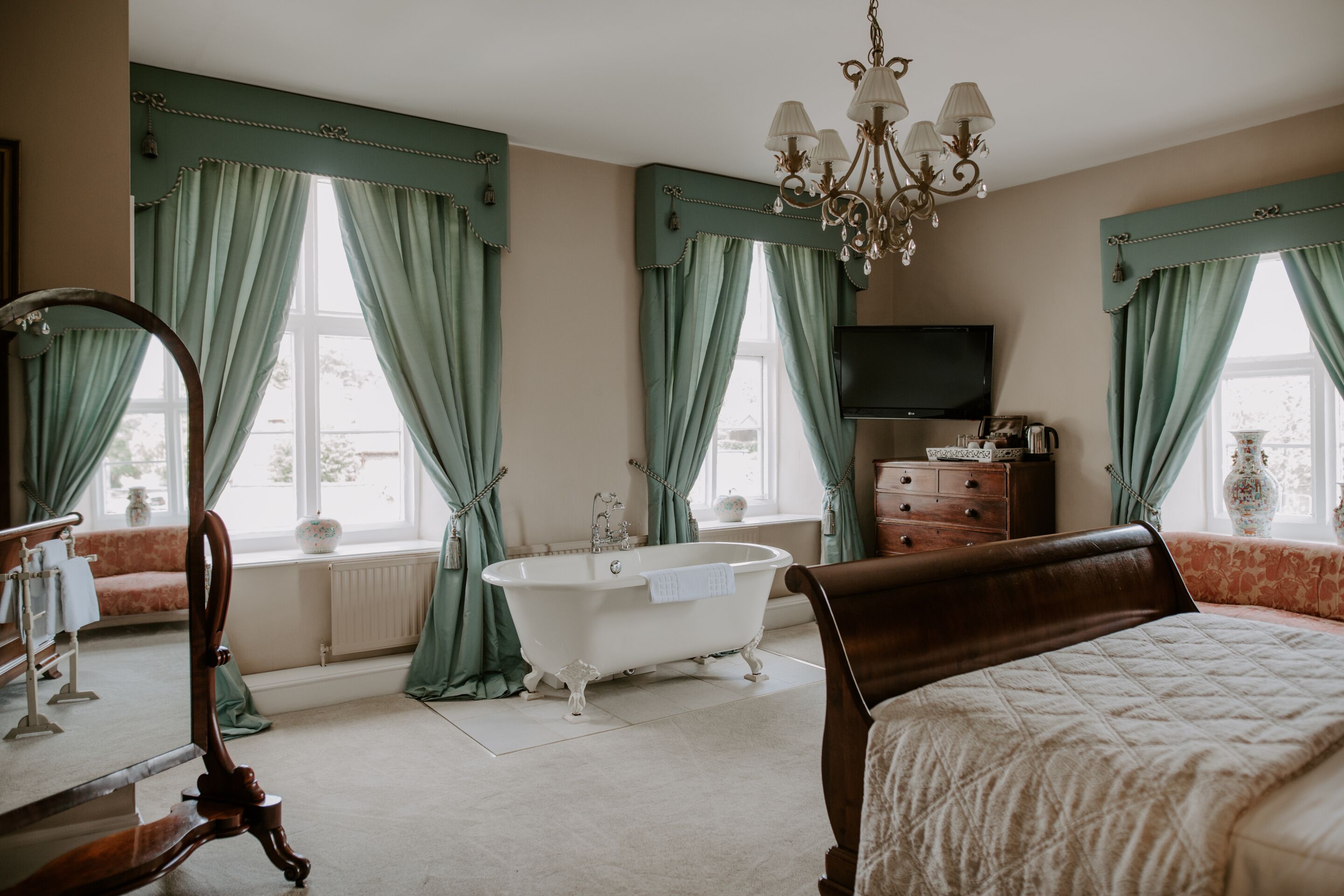 A bedroom with a large bed, a clawfoot bathtub, a dresser, and a television.